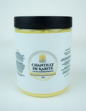 Pot ouvert de chantilly de karité fouettée, texture légère et onctueuse, vue en gros plan sur fond naturel. Mélange crémeux aux reflets beiges, évoquant la douceur des beurres d’Afrique.